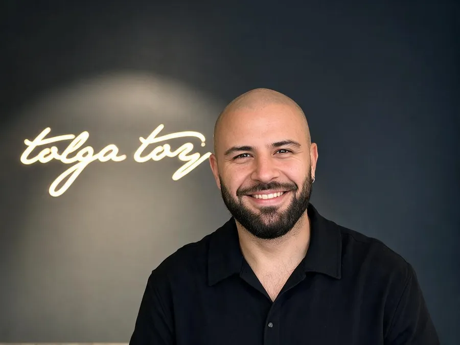 Tolga Toy vor dem Logo seines Salons in Düsseldorf